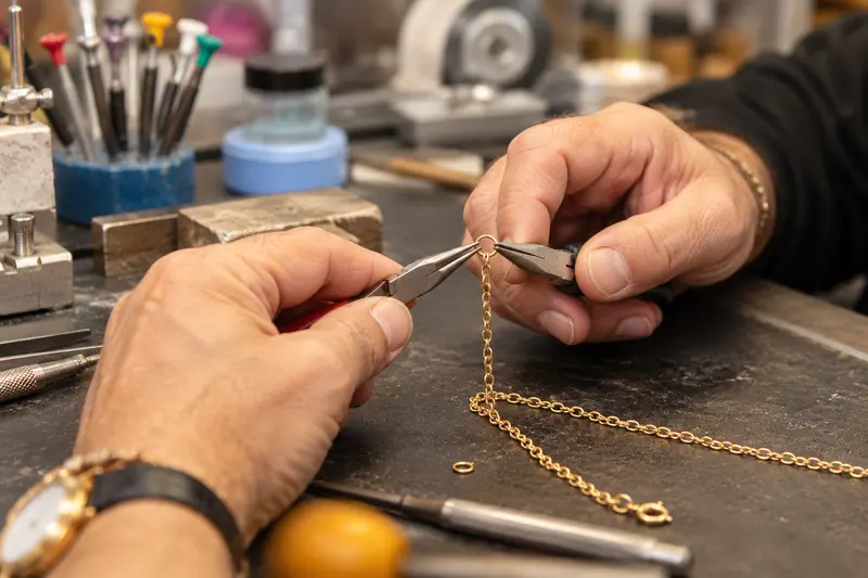 Zwei Hände halten mit zwei Zangen eine feine Goldkette, daneben liegen Schraubendreher und ein kleiner Ring.